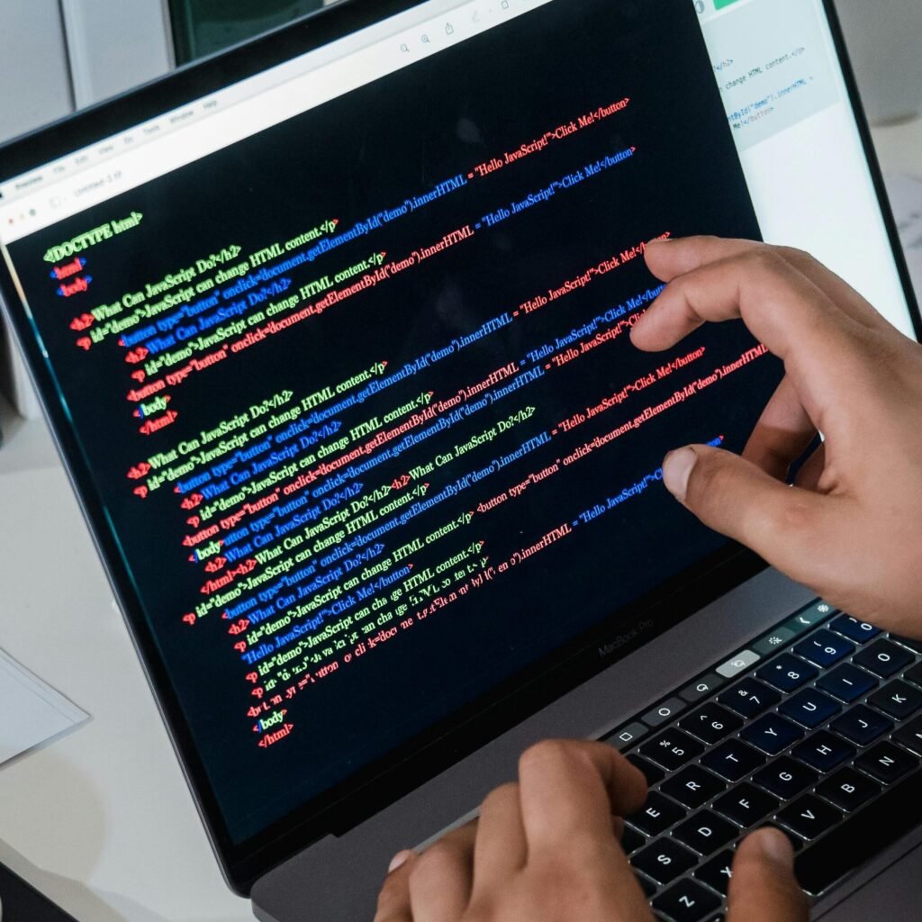 Close-up of a programmer pointing at a colorful code script on a laptop in an office setting.
